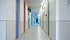 Krankenhausflur in zentraler Perspektive mit flächig angebrachtem Rammschutz und farbigen Türen zu einzelnen Patientenzimmern