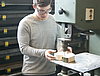 Man sieht einen jungen Mann, welcher mit einer Maschine ein Herz aus einem Holzblock schnitzt.