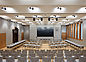 Das Bild zeigt einen großen Konferenzraum mit einem großen Bildschirm, hellgrauen Materialien und Holzdetails.