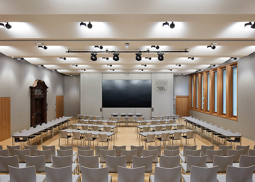 New Town Hall Bernau Great Hall The picture shows a big conference room featuring a big screen, light grey materials and wooden details.