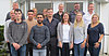 Man sieht 14 Auszubildende und Ausbilder, welche vor dem Eingang eines Gebäudes in Reihen für ein Gruppenfoto posieren.