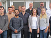 Man sieht 14 Auszubildende und Ausbilder, welche vor dem Eingang eines Gebäudes in Reihen für ein Gruppenfoto posieren.