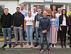 Man sieht etwa 20 Personen, welche vor einem Gebäude in mehreren Reihen für ein Gruppenfoto posieren.