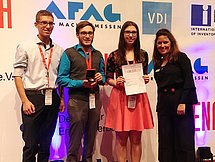 Gruppenbild der Gewinner Vier junge Personen posieren auf einem roten Teppich. Sie halten eine Ehrenurkunde und eine Medaille in einer Schatulle.