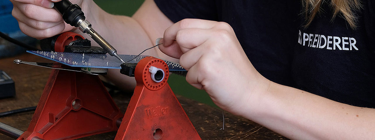 Eine Frau arbeitet sorgfältig an einer kleinen Leiterplatte