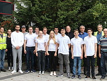 Gruppenfoto Auszubildende in Leutkirch Etwa 15 Auszubildende und Ausbilder posieren für ein Gruppenfoto in zwei Reihen. Im Hintergrund sieht man ein Gebäude und Bäume.