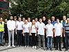 Etwa 15 Auszubildende und Ausbilder posieren für ein Gruppenfoto in zwei Reihen. Im Hintergrund sieht man ein Gebäude und Bäume.