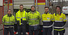 Zu sehen sind 5 Auszubildende in Feuerwehrschutzkleidung vor einem Feuerwehrauto