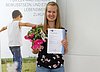Eine junge Dame präsentiert stolz ihr Prüfungszeugnis und einen Blumenstrauß.