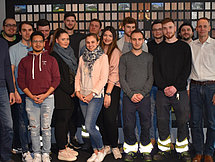 Abschlussgruppenfoto Man sieht eine Gruppe von etwa 20 Auszubildenden und Ausbildern, welche in Reihen für ein Gruppenfoto posieren.