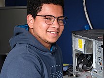 Ein junger Mann repariert einen Computer und lächelt in die Kamera