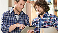 Pfleiderer Plus Partnerprogramm Twei Verarbeiter stehen zusammen und schauen auf ein Tablet.