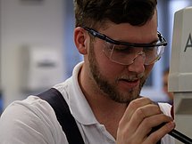 Ein Mann in Schutzkleidung bedient eine kleine Maschine