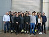 Etwa 20 Auszubildende und Ausbilder posieren vor einem Lagertor für ein Gruppenfoto.