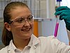 A young woman in protective gear observing a purple liquid in a glass tube