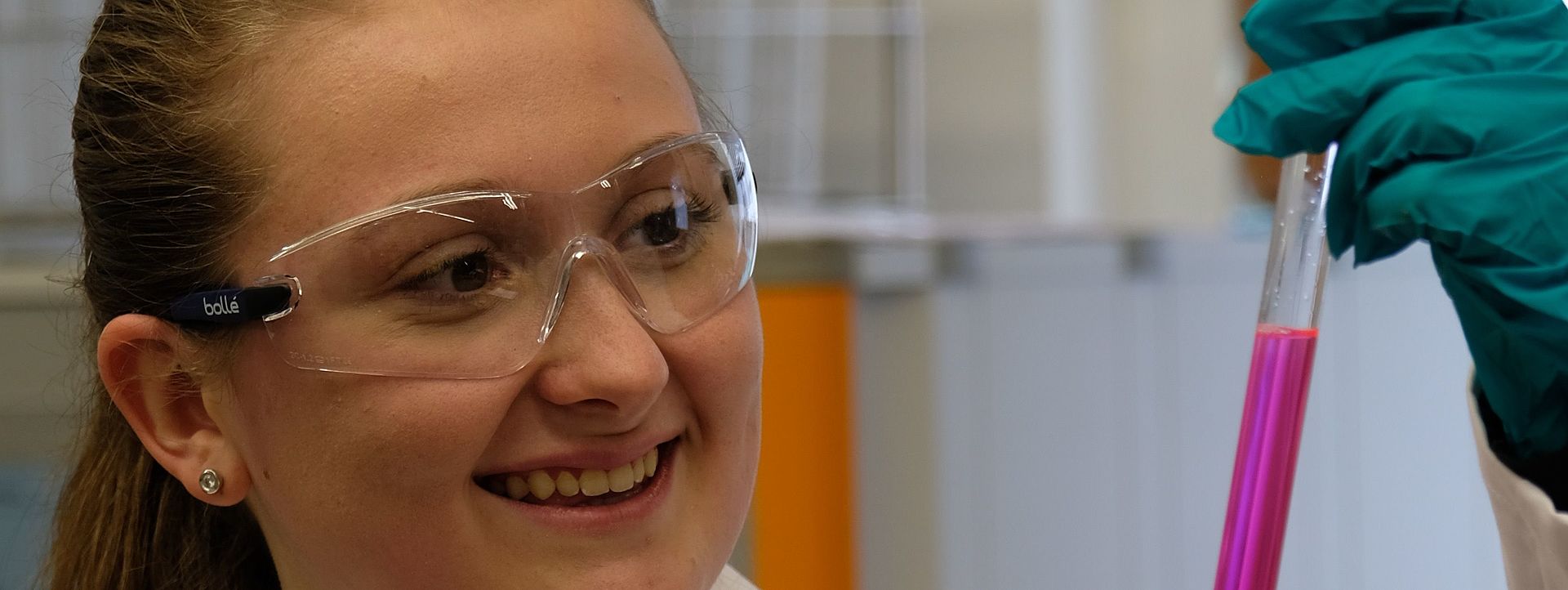 Symbolbild Chemielaborant Eine junge Frau in Schutzkleidung, die eine violette Flüssigkeit in einem Glasrohr beobachtet