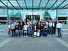 Etwa 30 Auszubildende und Ausbilder posieren vor einem gläsernen Gebäude für ein Gruppenfoto