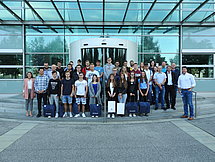 Gruppenfoto Auszubildende Etwa 30 Auszubildende und Ausbilder posieren vor einem gläsernen Gebäude für ein Gruppenfoto