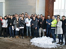 Gruppenfoto der Prüflinge Etwa 25 Auszubildende posieren mit ihren Ausbildern vor einem Lagertor.