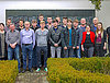 Etwa 20 Personen posieren draußen für ein Gruppenfoto vor einer Wand
