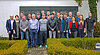 Etwa 20 Personen posieren draußen für ein Gruppenfoto vor einer Wand