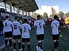 Fünf Fußballspieler stehen am Rand eines Sportplatzes vor einer Tribüne. Man sieht sie von hinten. Auf ihren Trikots steht "Gütersloh".