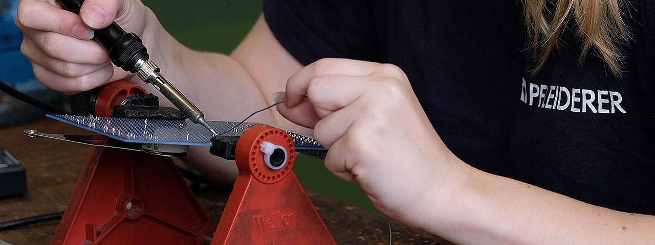 Symbolbild Elektroniker Das Bild zeigt eine Frau, die sorgfältig an einer Leiterplatte arbeitet