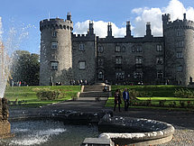 Schloss in Dublin Man sieht einen alten Brunnen vor einem imposanten britischen Schloss an einem sonnigen Tag.