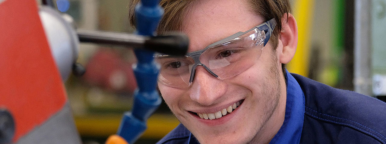 Ein junger Mann in Schutzkleidung bedient eine Maschine zur Holzbearbeitung