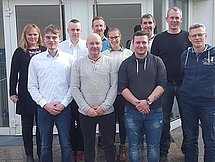 Gruppenfoto der Absolventen und ihren Ausbildern Eine Gruppe an Absolventen und ihren Ausbildern posiert vor einem Gebäude für ein Gruppenfoto in drei Reihen