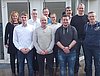Eine Gruppe an Absolventen und ihren Ausbildern posiert vor einem Gebäude für ein Gruppenfoto in drei Reihen
