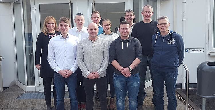 Gruppenfoto der Absolventen und ihren Ausbildern Eine Gruppe an Absolventen und ihren Ausbildern posiert vor einem Gebäude für ein Gruppenfoto in drei Reihen