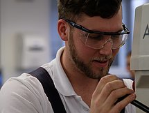Ein junger Mann in Schutzkleidung bedient eine kleine Maschine