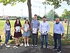 4 Auszubildende zeigen stolz ihre Prüfungsurkunden. Neben ihnen stehen ihre Ausbilder. Sie befinden sich an einem Sportplatz.