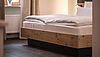 Frisch gemachtes Hotelbett mit weißen Bezügen in natürlichem Ambiente von Holzoberflächen und hellen Cremetönen