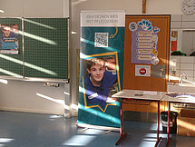 Pfleiderer Banner Man sieht einen Austellbanner von Pfleiderer in einem Klassenzimmer. Der Banner zeigt einen Auszubildenden und einen QR-Code.