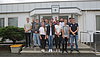 Man sieht 14 junge Leute, welche für ein Gruppenfoto in zwei Reihen vor einem Gebäude posieren.