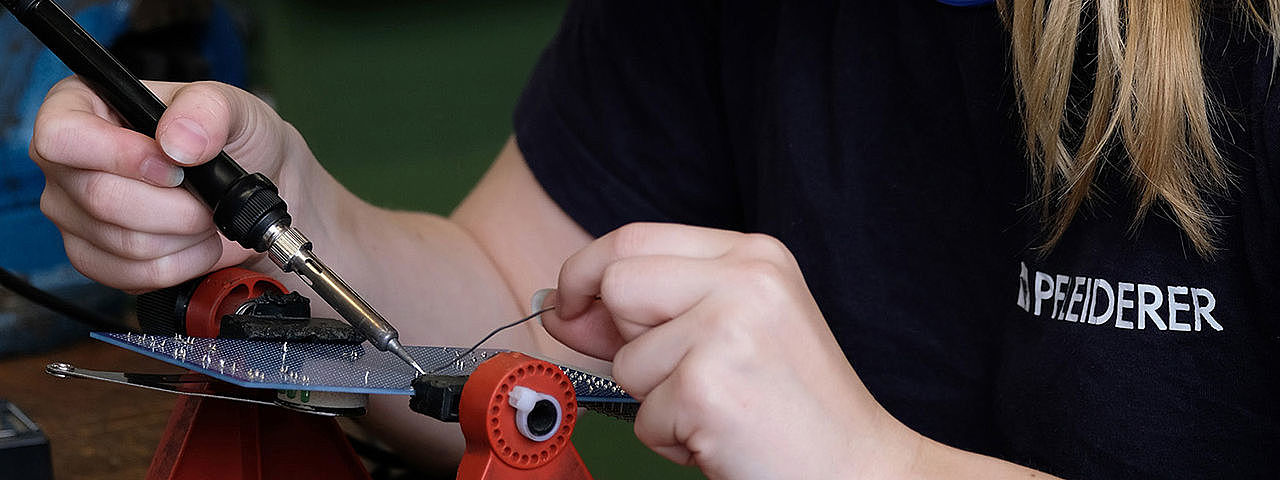 Eine junge Frau arbeitet sorgfältig an einer Leiterplatte