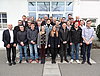 Man sieht eine Gruppe von Auszubildenden und Ausbildern, welche vor dem Eingang eines Gebäudes für ein Gruppenbild in Reihen stehen.