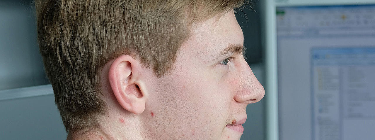 Symbolbild Informatikkaufmann A man in a red sweater sits in front of his PC