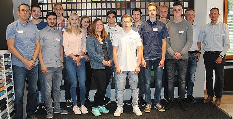 Gruppenfoto der Absolventen Man sieht etwa 15 Auszubildende und Ausbilder, welche vor einer Wand mit Probematerialien für ein Gruppenfoto posieren.