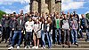 Etwa 30 Auszubildende posieren in Alltagskleidung auf einer Treppe vor einem alten Monument