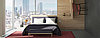 L'immagine mostra una camera d'albergo con un letto di fronte a grandi finestre ad angolo. Per le pareti e i mobili sono stati utilizzati diversi materiali di alta qualità.