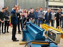 Begutachtung der Maschinerie Einige Auszubildende gucken sich eine blau-gelbe Industriemaschine in einer Halle an