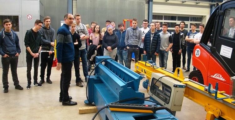 Begutachtung der Maschinerie Einige Auszubildende gucken sich eine blau-gelbe Industriemaschine in einer Halle an