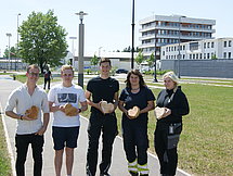 Auszubildende mit Holzherzen Fünf Auszubildende posieren mit ihren gefertigten Holzherzen. Sie stehen auf einem Weg vor einer Wiese und es ist sehr sonnig.