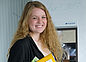 The picture shows a young woman with long blond curls smiling directly into the camera.