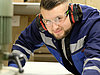 The picture shows a man in protective gear operating big machinery and looking straight into the camera