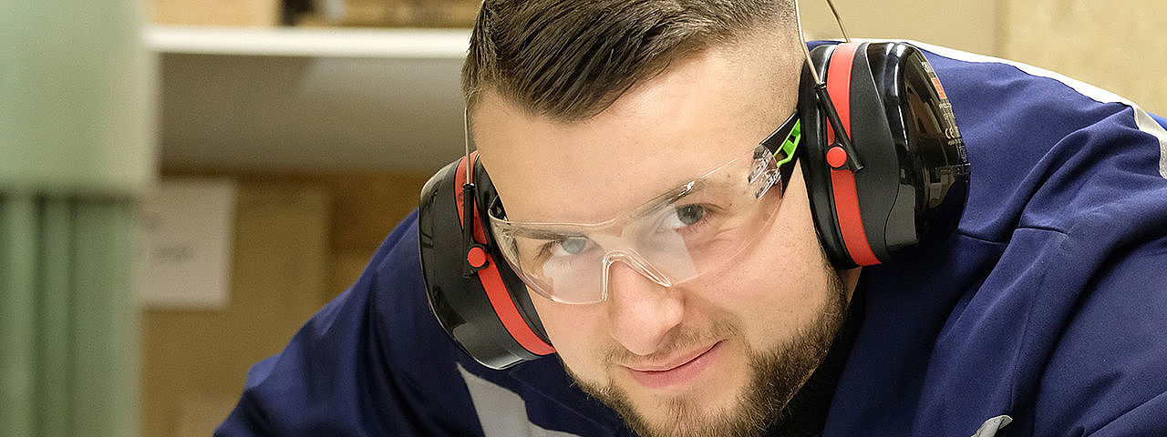 Symbolbild Anlagenführer Das Bild zeigt einen Mann in Schutzkleidung, der große Maschinen bedient und direkt in die Kamera schaut