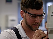 Ein junger Mann in Schutzkleidung bedient eine kleine Maschine